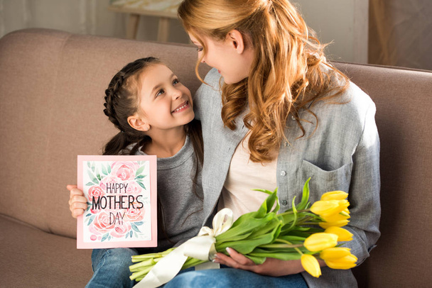 Glückliche Mutter und Tochter mit gelben Tulpen und Glückwunschkarte zum Muttertag - Foto, Bild
