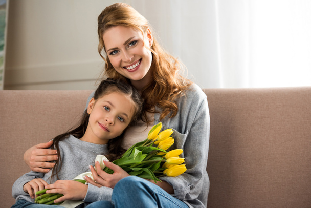 happy mother and daughter with yellow tulips sitting together and smiling at camera - Φωτογραφία, εικόνα