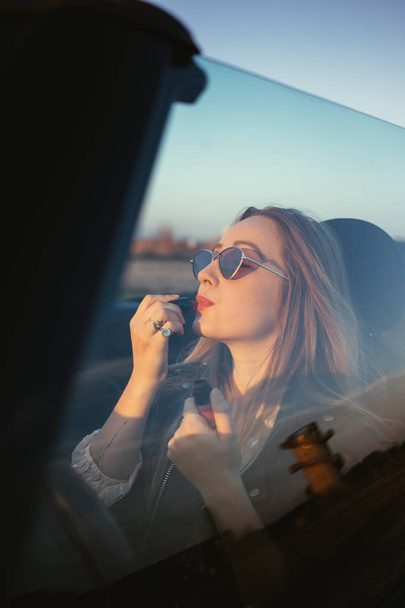 portrait of young woman applying make up in car at sunset - 写真・画像