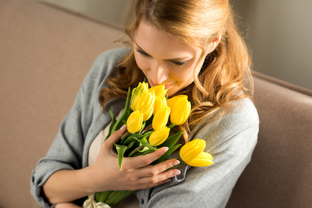 szép mosolygó fiatal nő otthon tartja a sárga tulipánok - Fotó, kép