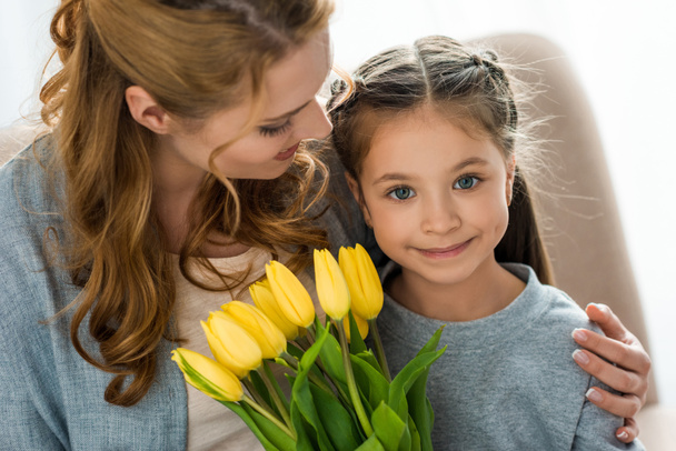 happy mother looking at cute daughter with yellow tulips smiling at camera - Foto, immagini