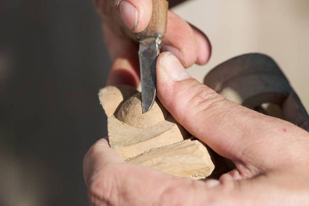 Close-up van een man, hout snijwerk. Alleen handen, gereedschappen en het houten stuk zijn zichtbaar op de foto. - Foto, afbeelding