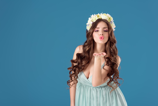 krásná dívka s květy věnec na hlavu odesílání vzduchu polibek izolované na modré - Fotografie, Obrázek