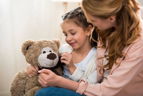 beautiful happy mother and daughter playing with teddy bear at home - Photo, Image
