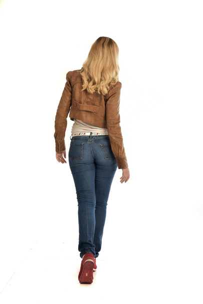 po celé délce portrét blond dívka, která nosí hnědé sako a džíny. představovat stojící na bílém pozadí. - Fotografie, Obrázek