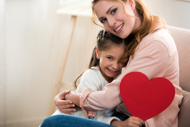 Szczęśliwa matka i córka z czerwone serce symbol przytulanie i uśmiecha się do kamery - Zdjęcie, obraz