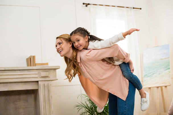 happy mother piggybacking adorable little daughter at home - Foto, Bild
