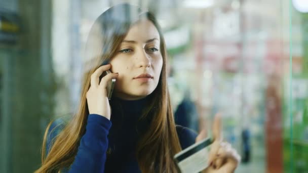 An attractive woman speaks on the phone, looks through the glass case in the store. Shopping Choice and Shopping Concept - Materiał filmowy, wideo