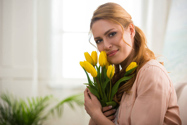 happy young woman holding yellow tulips and smiling at camera - Photo, Image