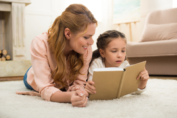 glückliche Mutter und Tochter liegen auf Teppich und lesen gemeinsam Buch - Foto, Bild
