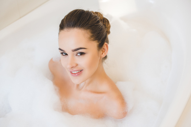 smiling young woman taking bath with foam at home - Foto, Bild