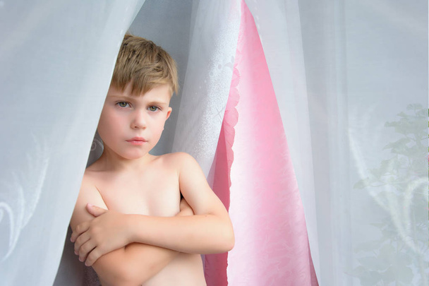 Ένα μικρό αγόρι χωρίς ρούχα στέκεται δίπλα στο παράθυρο - Φωτογραφία, εικόνα