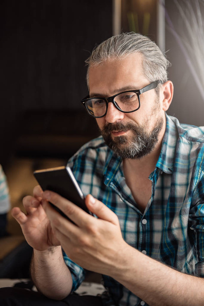 Man with glasses and beard using smart phone at home - Fotó, kép