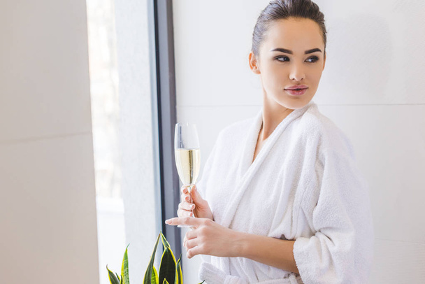 portrait of beautiful woman in bathrobe with glass of champagne at home - Foto, imagen