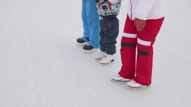 Los primeros pasos de un niño pequeño en patines. Mamá y papá enseñan a un niño a patinar y sostener sus manos sobre el hielo. Vacaciones familiares y actividades al aire libre
 - Metraje, vídeo