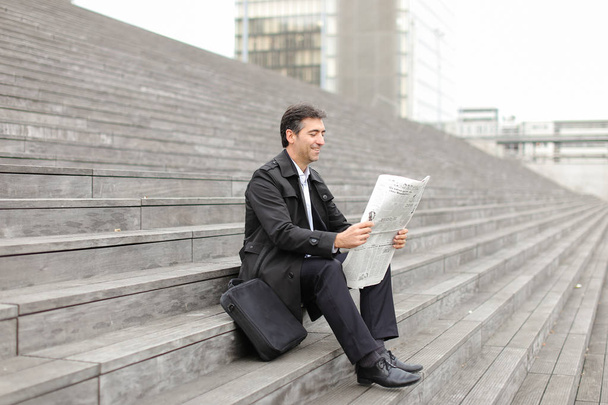 tutor de negócios do sexo masculino sentado nas escadas e ler jornal
 - Foto, Imagem