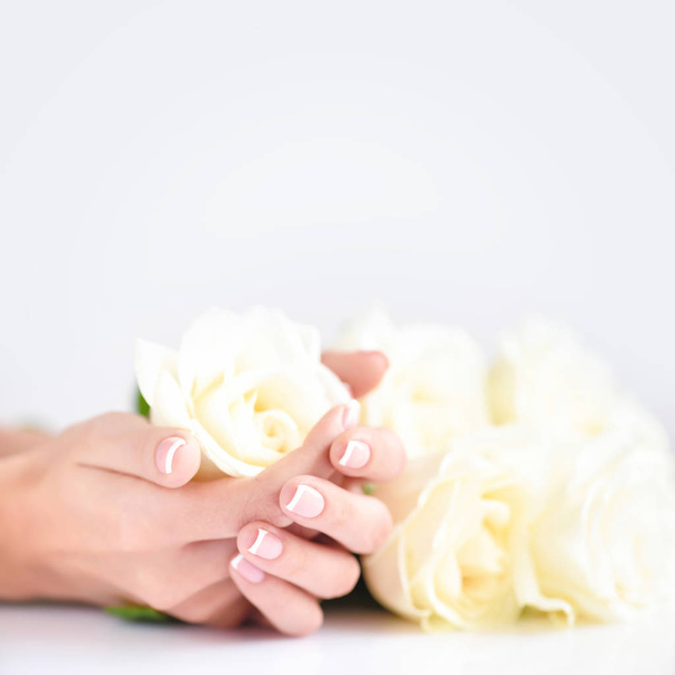 Mani di una donna con bella manicure francese e rose bianche - Foto, immagini