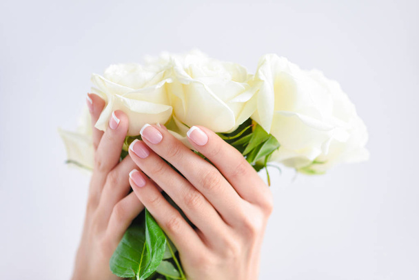 Egy gyönyörű francia manikűrös nő kezei és fehér rózsacsokor. - Fotó, kép