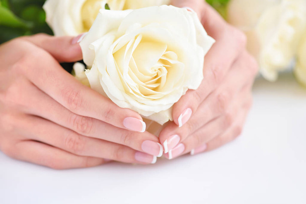 Hände einer Frau mit schöner französischer Maniküre und weißen Rosen - Foto, Bild