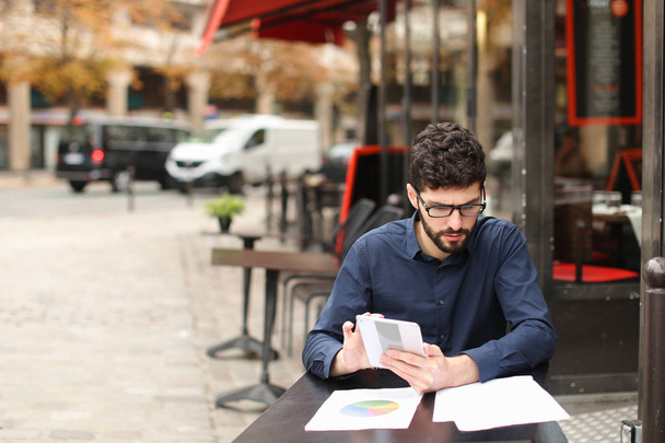 Бизнесмен спорит на смартфоне и читает газеты в кафе
 - Фото, изображение
