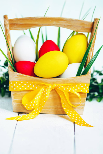 Easter spring composition, basket with painted colorful eggs and grass around. Close up portrait on sky background. - Фото, изображение