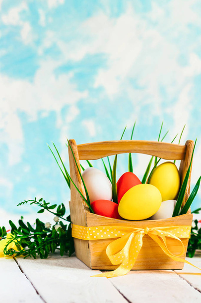 Easter spring composition, basket with painted colorful eggs and grass around. Close up portrait on sky background. - Photo, image