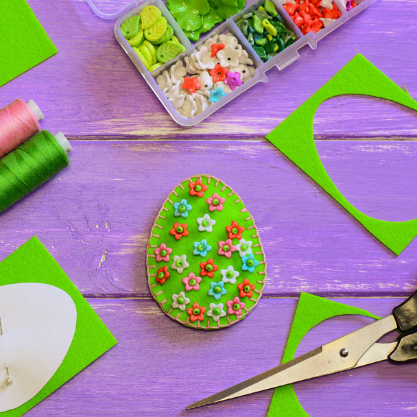 プラスチック製の花の創造的なイースターエッグのデコレーション。花柄、はさみ、紫の木製のテーブルに紙のテンプレートと卵を感じた。卵工芸。楽しい簡単なミシン。手の縫製プロジェクト。初心者のためのアイデアを縫製。幼児のためのミシン - 写真・画像