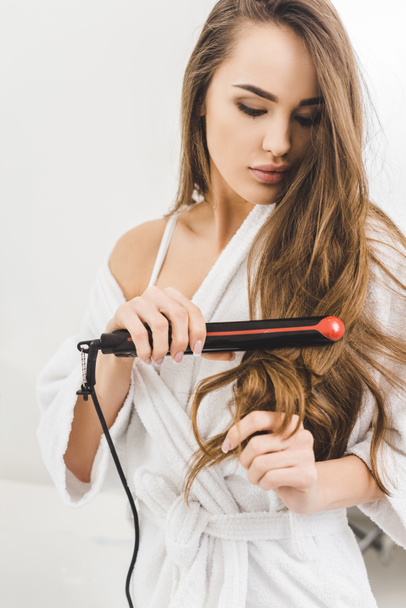 portrait of woman straightening hair with hair straightener - Фото, зображення