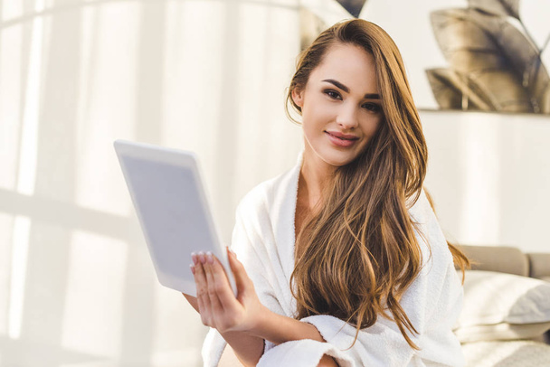 portrait of young woman in bathrobe with tablet sitting on bed at home - Foto, immagini