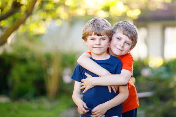 zwei kleine aktive Schulkinder Jungen, Zwillinge und Geschwister, die sich an einem Sommertag umarmen - Foto, Bild