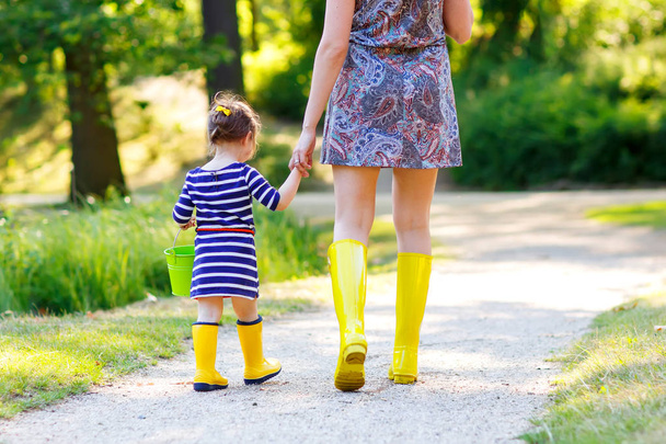 Matka i dziecko śliczny maluch w żółte kalosze, Rodzina spojrzenie, w lato park. Piękna kobieta i córka Ładna dziewczyna, chodzenie ze sobą - Zdjęcie, obraz