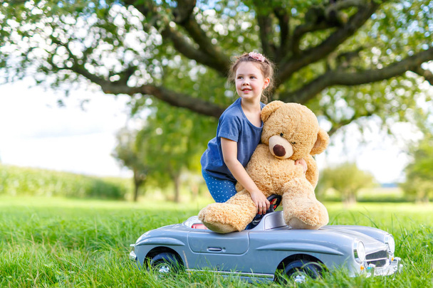 Małe przedszkola dziecko dziewczynka jazda samochodem duże zabawki i zabawy z gry z duże pluszowe zabawki Miś - Zdjęcie, obraz