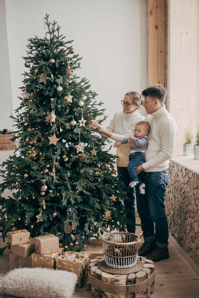 portrait of young couple with baby boy standing near Christmas tree - Fotó, kép