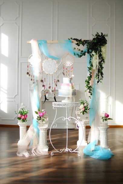 Pastel de boda cerca de un arco de boda con columnas en un interior blanco con chimenea
 - Foto, Imagen
