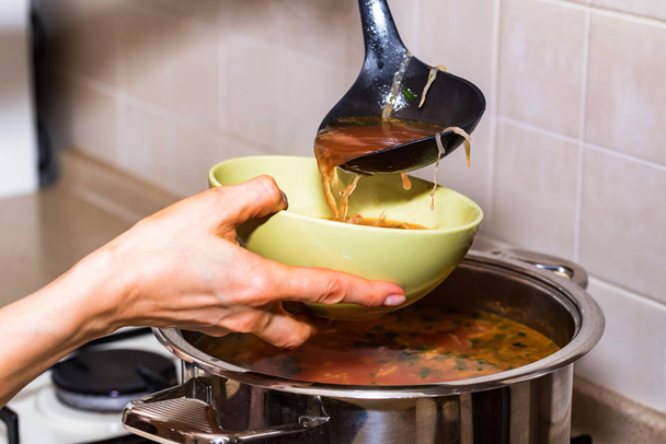 Hand pours borscht or red vegetable soup in bowl - Fotoğraf, Görsel