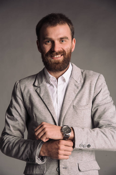 Portrait of smiling man with beard in white shirt and grey jacket isolated on gray studio background posing to the camera - Φωτογραφία, εικόνα