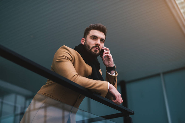 bearded happy young man with in beige jacket talking on mobile phone - Photo, Image
