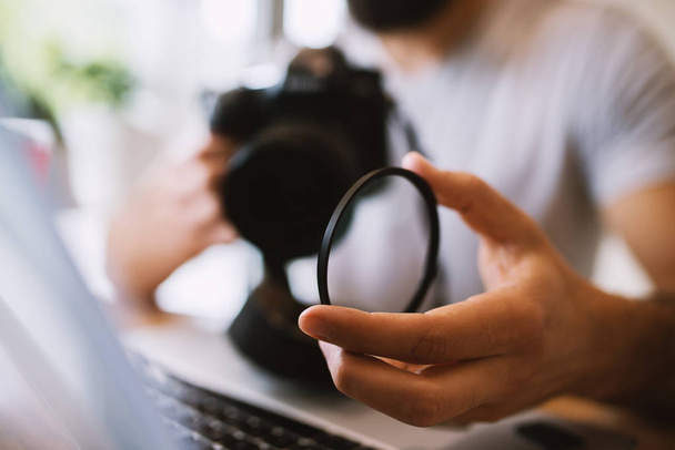 man opstijgen lens van professionele camera terwijl het gebruiken van laptop - Foto, afbeelding