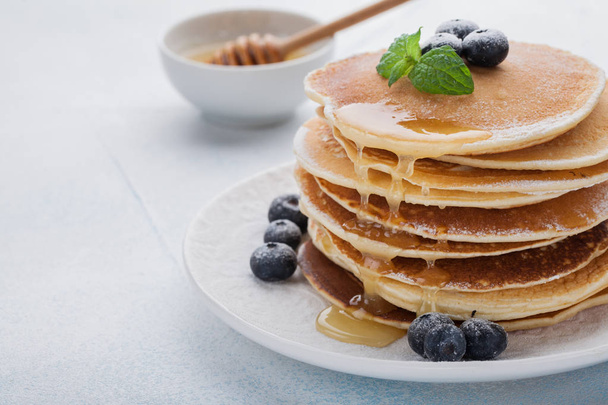 A stack of delicious pancakes with honey and blueberries on a light blue background. with copy space - Foto, Imagem