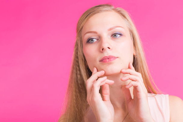 Beautiful blonde girl portrait with hands for cosmetic concept over pink background. - Foto, Bild