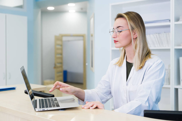Lachende verpleegkundige met laptop plannen van afspraak voor mannelijke patiënt bij de receptie - Foto, afbeelding