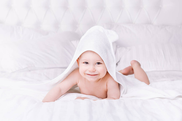 Adorably miminko leží na bílý ručník v posteli. Šťastné dětství a zdravotnické koncepce. - Fotografie, Obrázek