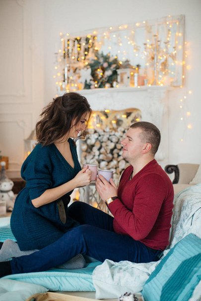 Happy Young beautiful couple with cups in christmas studio interier  - Photo, image