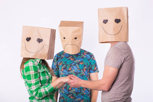 Love triangle, jealousy and unrequited love concept - woman and man with bags over heads holding hands and another man is angry. - Photo, Image