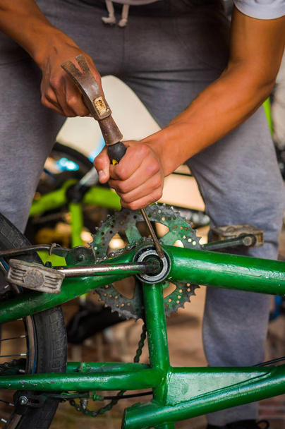 Крупный план человека, работающего молотком над педалью велосипеда в мастерской в процессе ремонта
 - Фото, изображение
