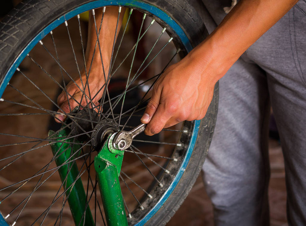 Close up of bicycle mechanic in a workshop in the repair process of the wheel with a wrench - Фото, изображение