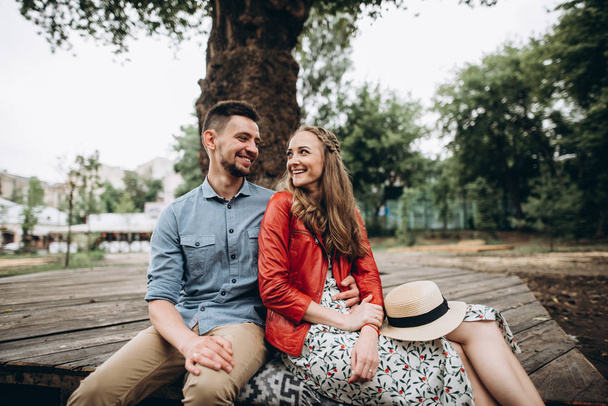 Молодий веселий хлопець і дівчина проводять час разом, сидячи біля дерева в парку. Історія кохання
 - Фото, зображення