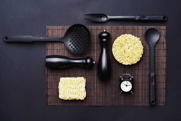 Διάταξη των αξεσουάρ κουζίνας και τα στιγμιαία noodles σε μαύρο φόντο. Το Top view. - Φωτογραφία, εικόνα