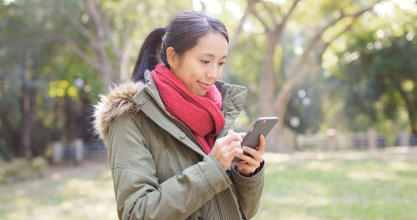 Женщина смотрит на мобильный телефон в парке
  - Фото, изображение