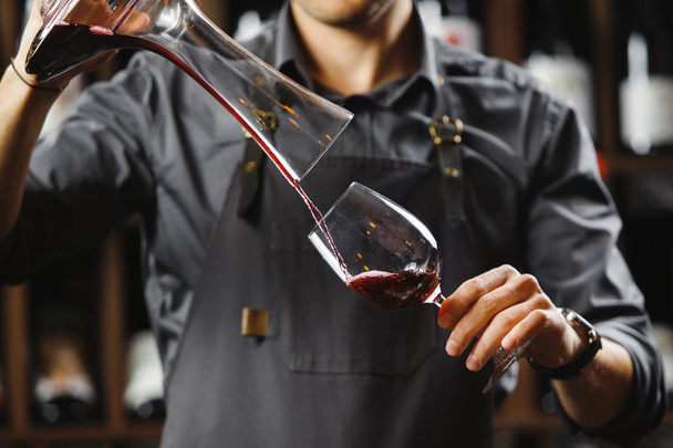 Bartender pours red wine in glass from big transparent vessel - Zdjęcie, obraz